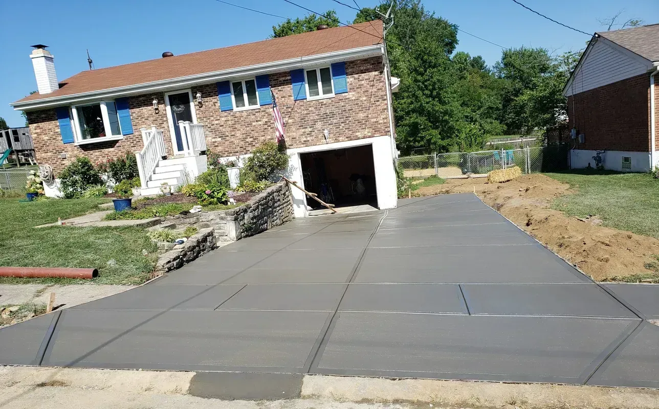 Newly poured concrete driveway leading up to a brick house with an attached garage.