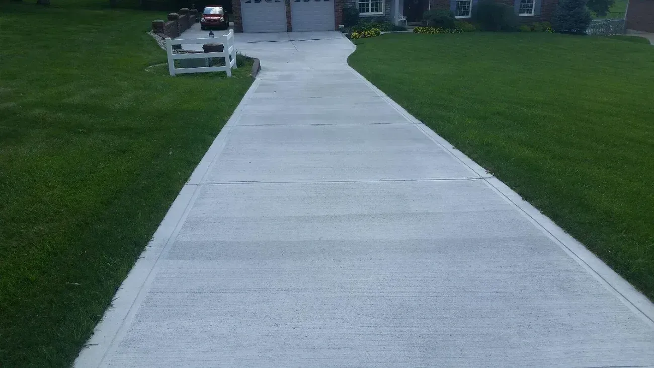 Concrete driveway leading to a garage and house, surrounded by green grass.