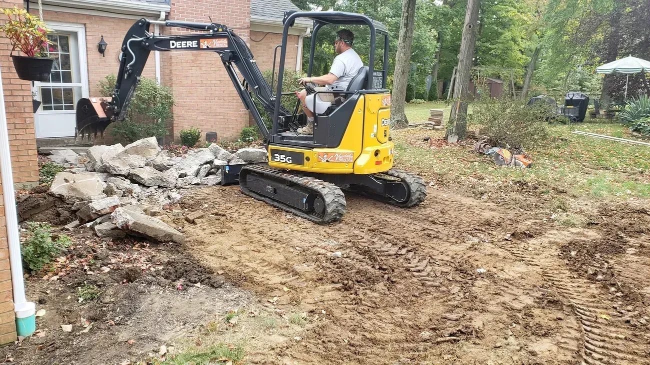 Man operating a yellow excavator removing debris near a brick building.