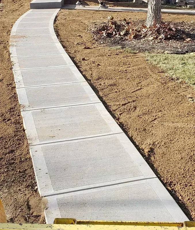 Concrete sidewalk curving through a dirt yard.