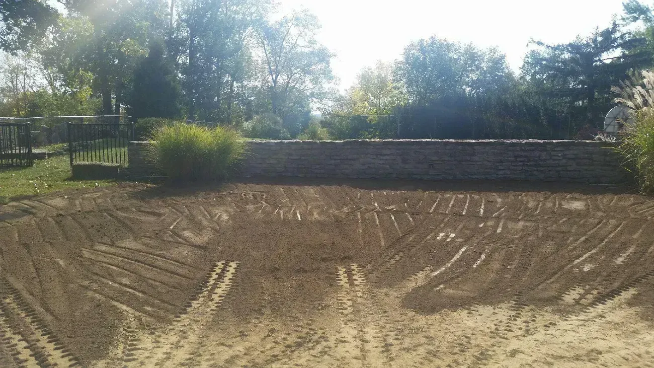 An excavated earthen area with a low wall in the background, trees, and blue sky.