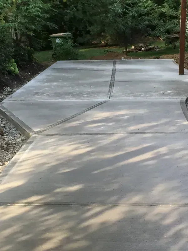 Newly poured concrete driveway with expansion joints and access to a wooded area.
