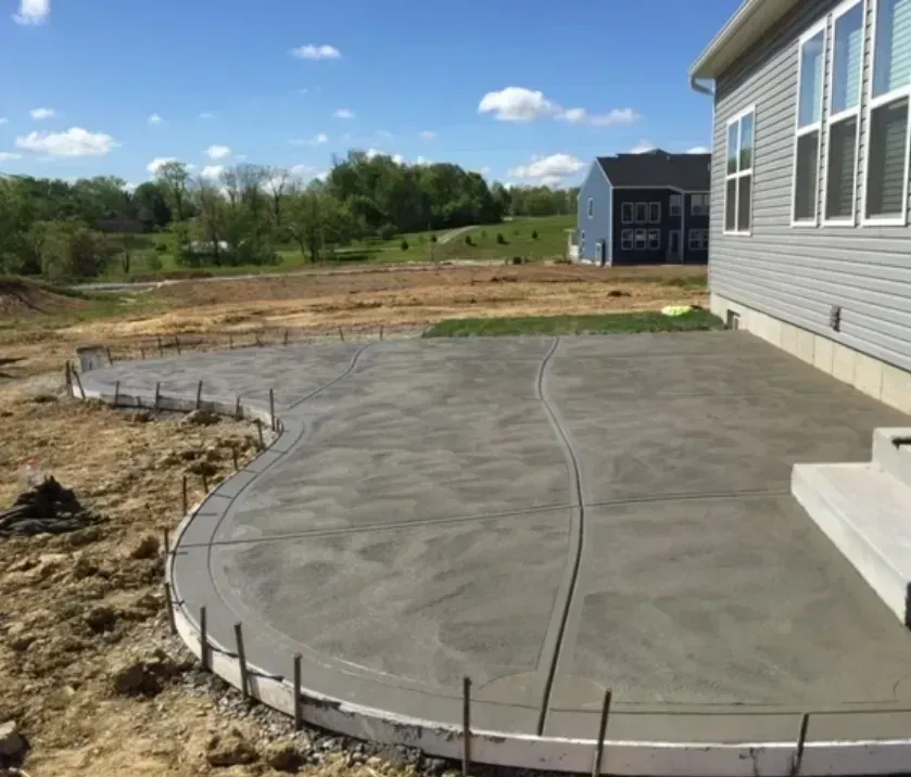 Newly poured concrete patio next to a house under construction; curved edges.
