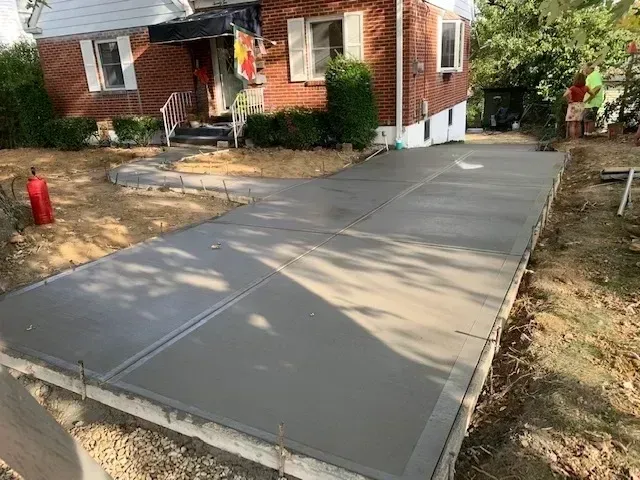 Freshly poured concrete driveway in front of a brick house with a person in the background.