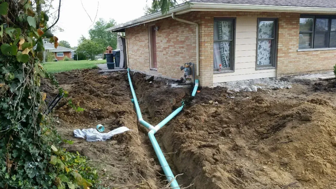 Excavated yard with turquoise drain pipes leading from a house with brick exterior; a cloudy day.
