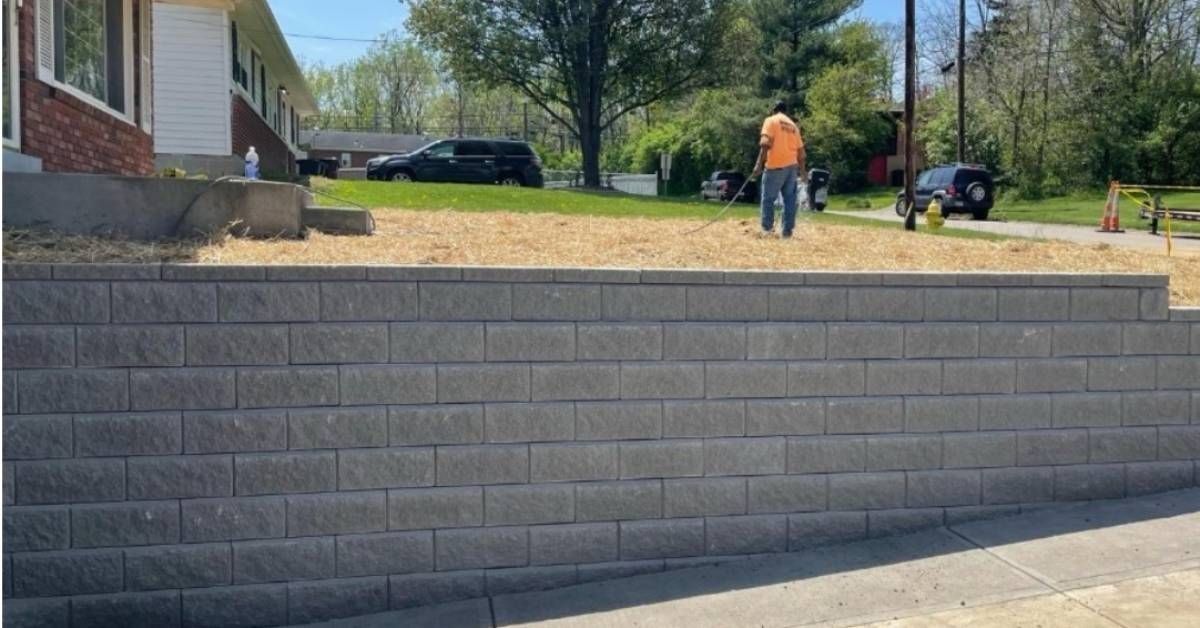 Gray brick retaining wall in front of a house, with a man standing on top.