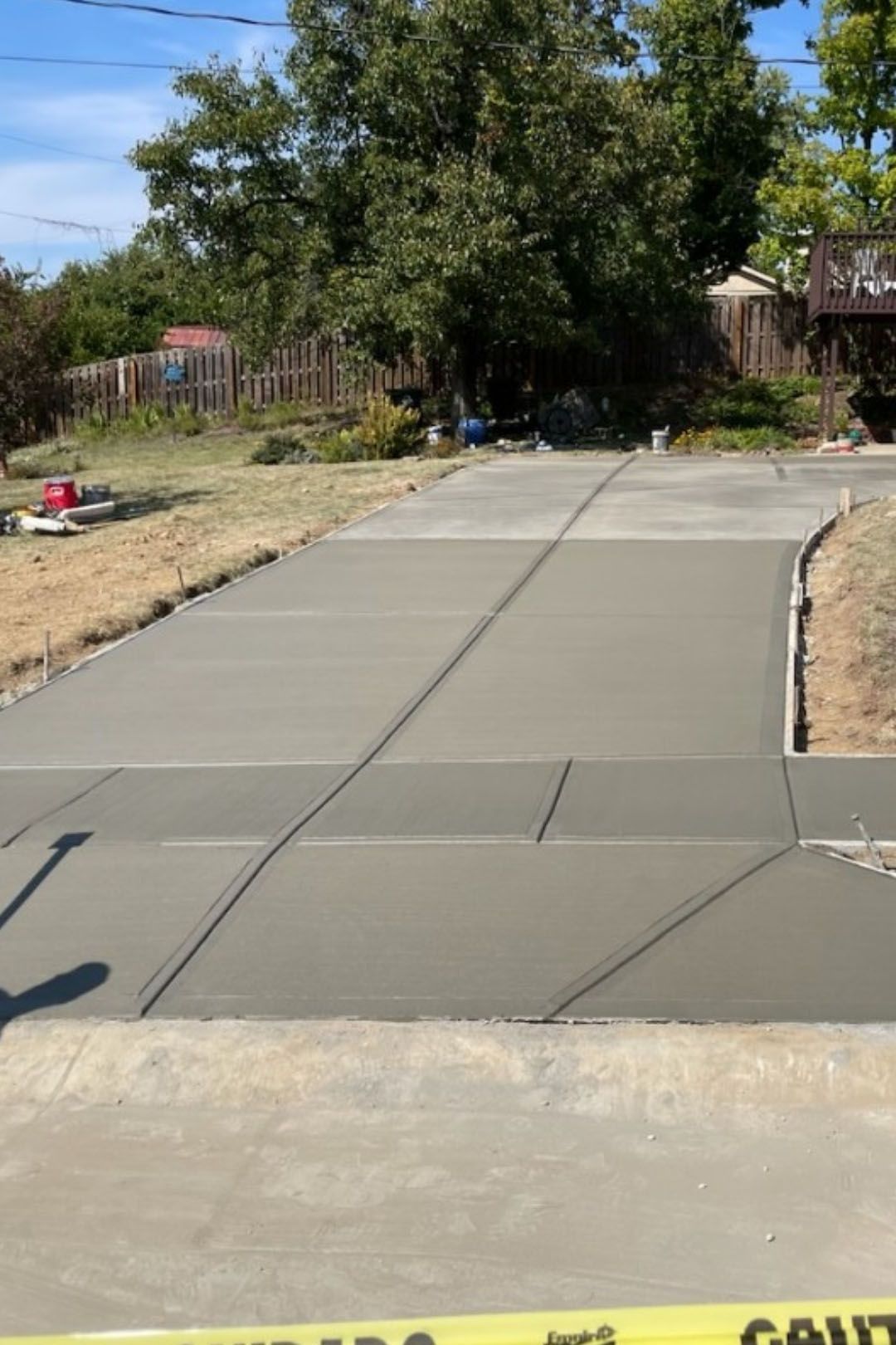 Freshly poured concrete driveway. Gray, rectangular slabs with joints, extending into a residential area with trees.