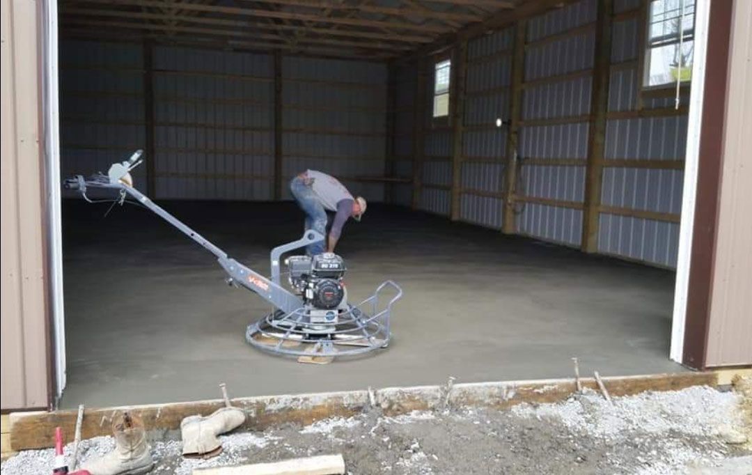 Man operating a power trowel, smoothing concrete floor inside a metal building.