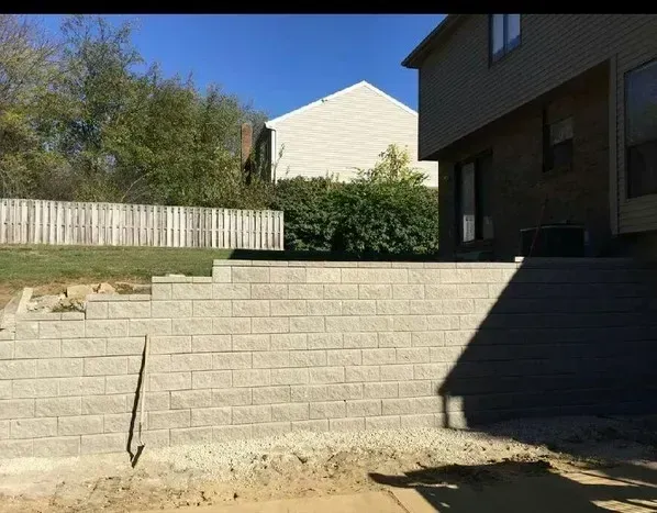 Retaining wall made of beige blocks, bordering a yard. A light-colored house is visible in the background.