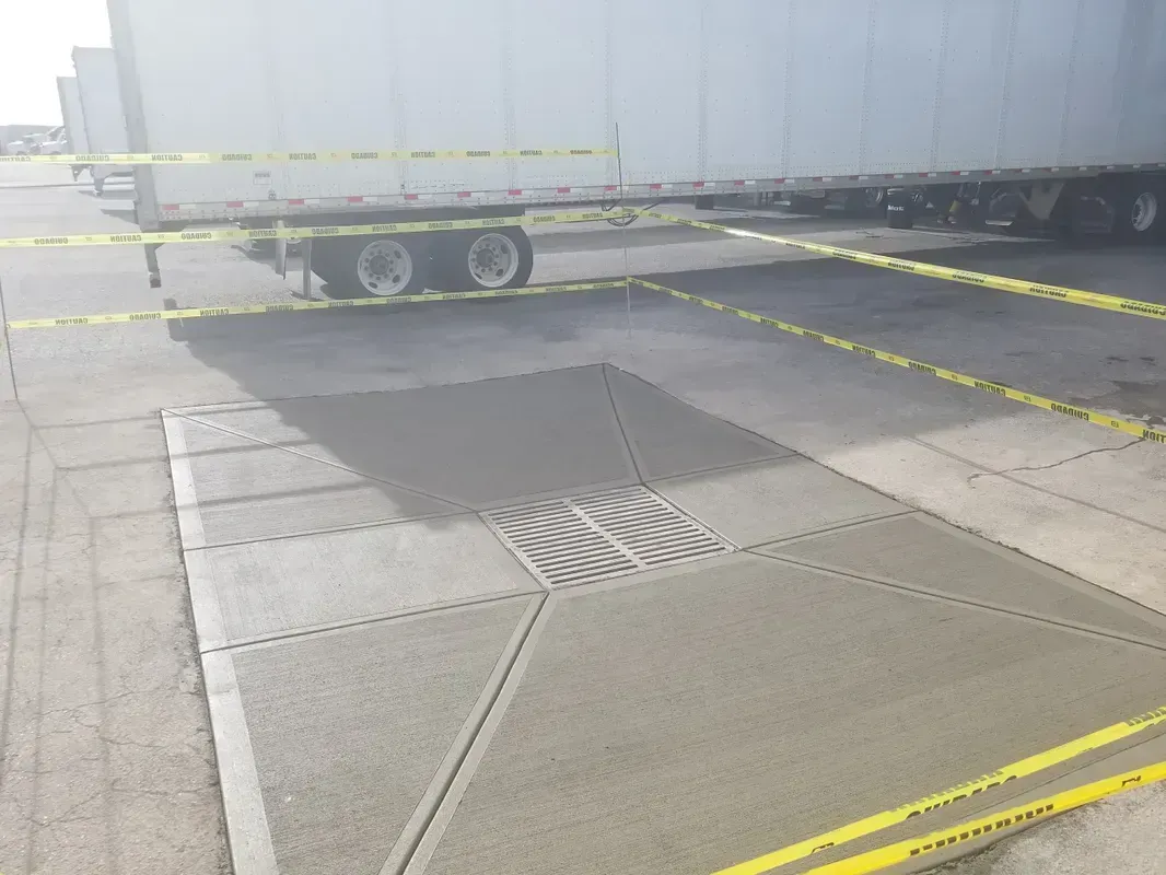 Concrete slab repair under a parked semi-trailer; yellow caution tape surrounds the area.