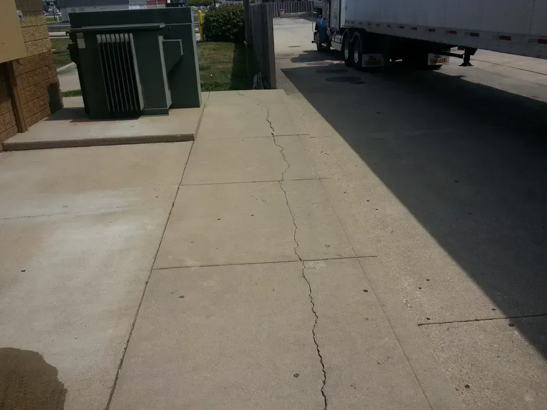 Concrete sidewalk with cracks; utility box on left, truck on right.