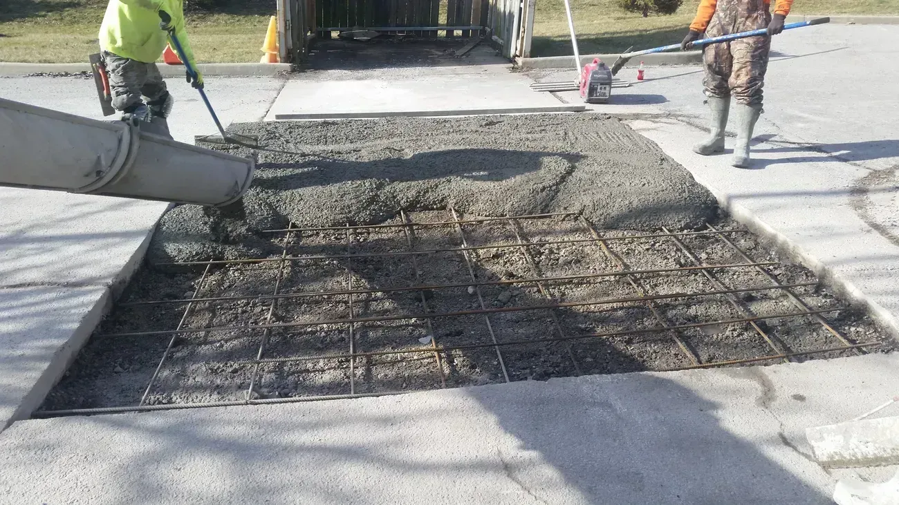 Concrete being poured into a sidewalk repair. Workers use tools to spread the fresh cement.