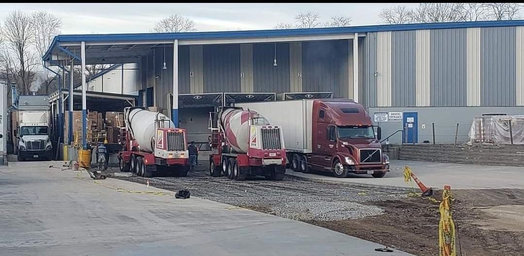 Trucks at a loading dock with concrete mixers and a semi-trailer in an industrial setting.