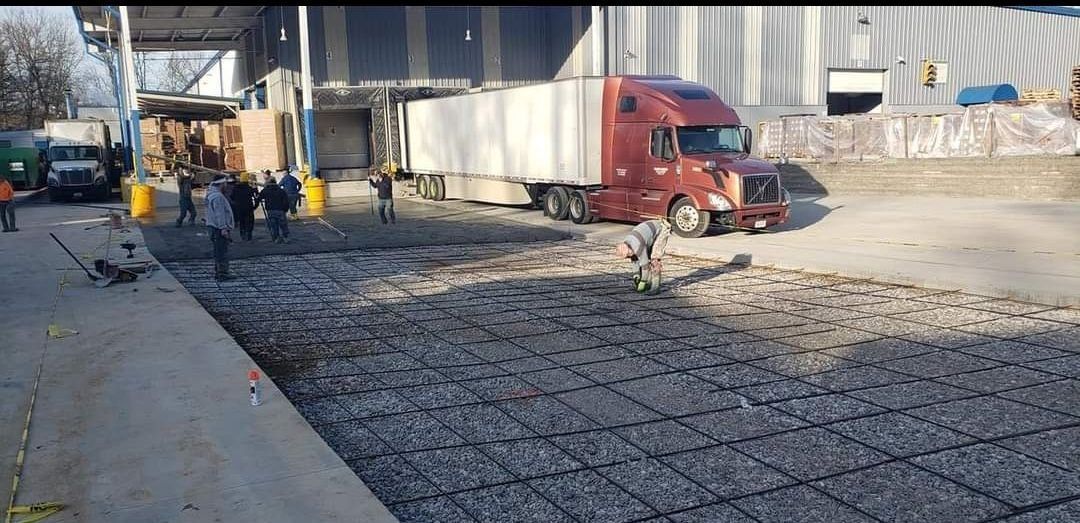 Construction workers preparing concrete for pouring near a semi-truck at a loading dock.