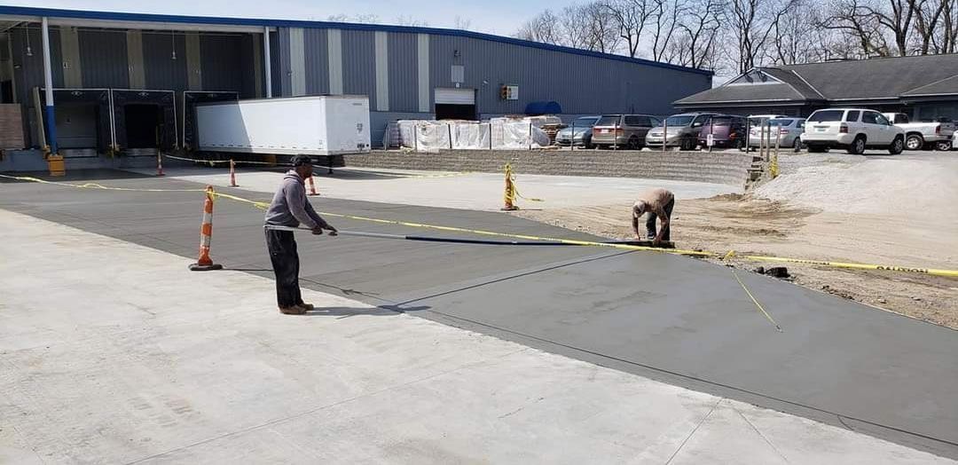 Two workers paving a driveway at a loading dock with the building in the background.