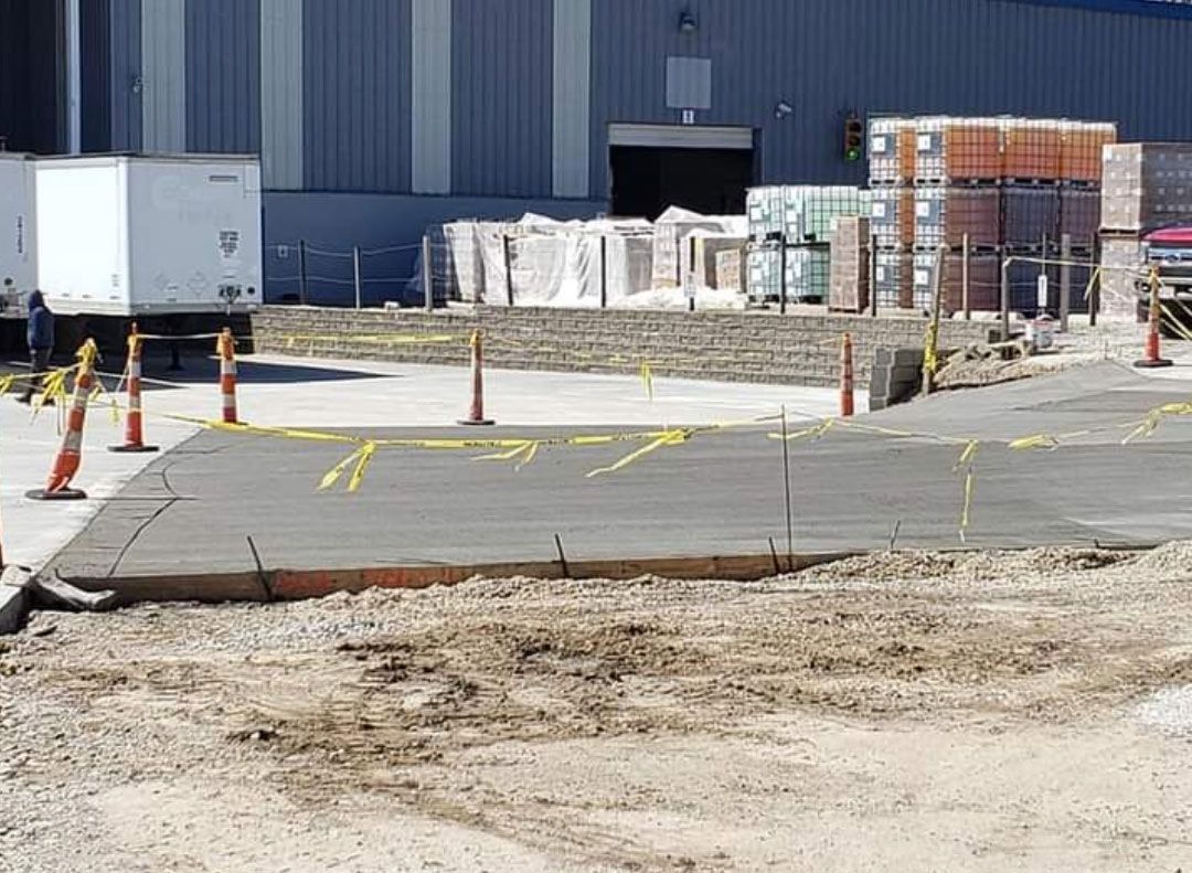 Concrete ramp with yellow arrows, orange cones, and a truck near a building.