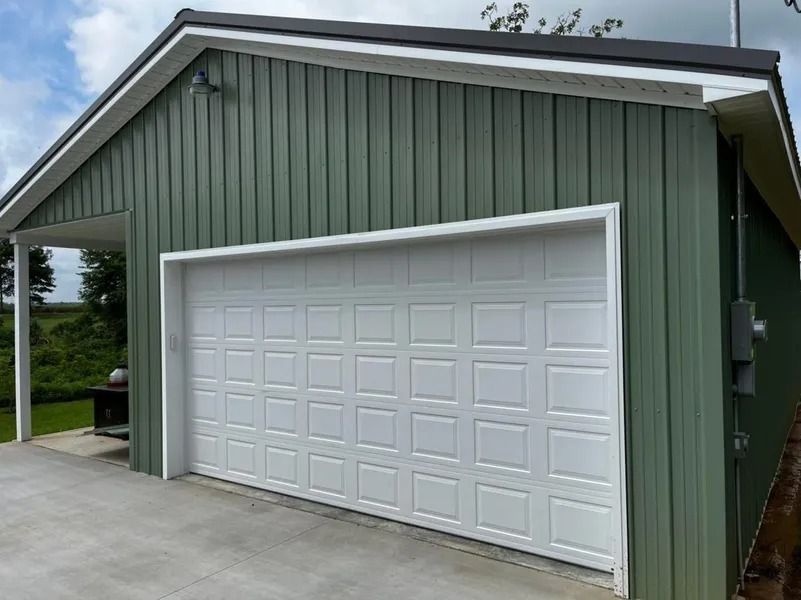 Green metal building with white garage door and concrete pad.