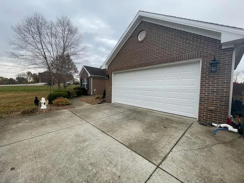 Brick house with white garage door and concrete driveway on a cloudy day.