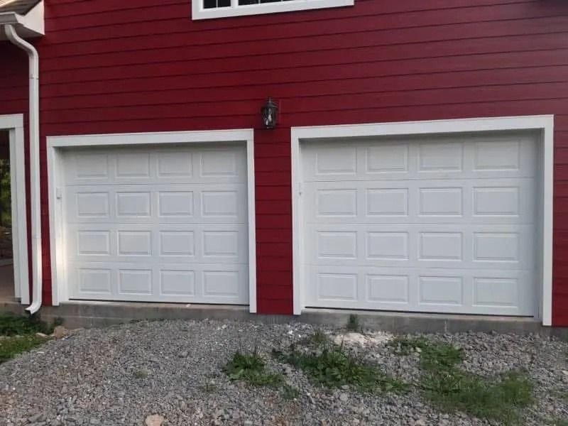 Red building with two white garage doors and gravel ground.