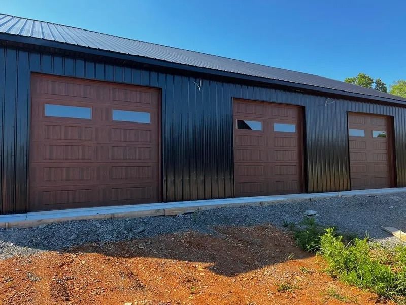 Black metal garage building with three brown garage doors, blue sky background.