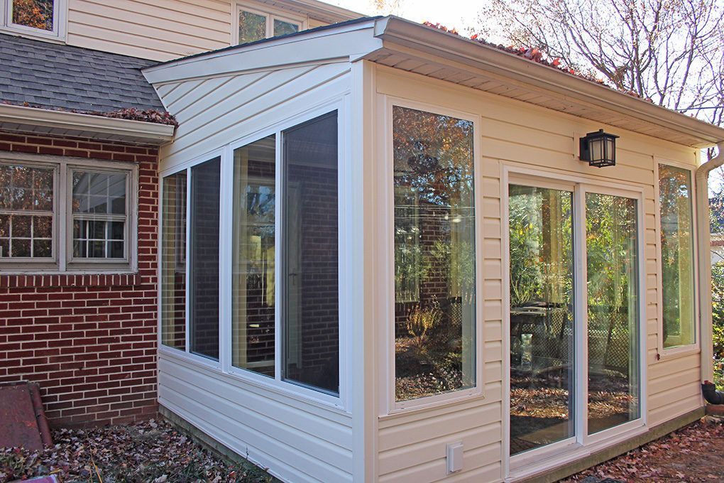 Sunroom addition with large windows and sliding glass doors, attached to a brick house.