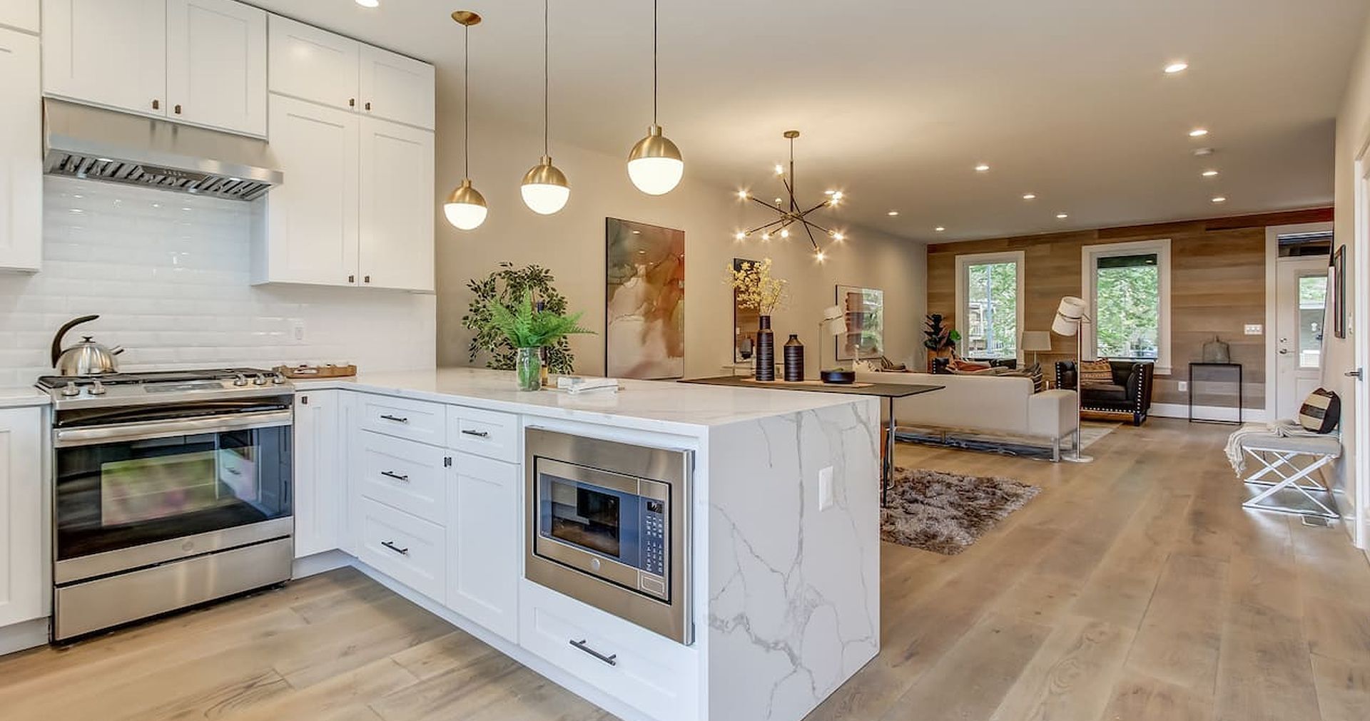 Modern kitchen with white cabinets, marble island, stainless steel appliances, and wood flooring.
