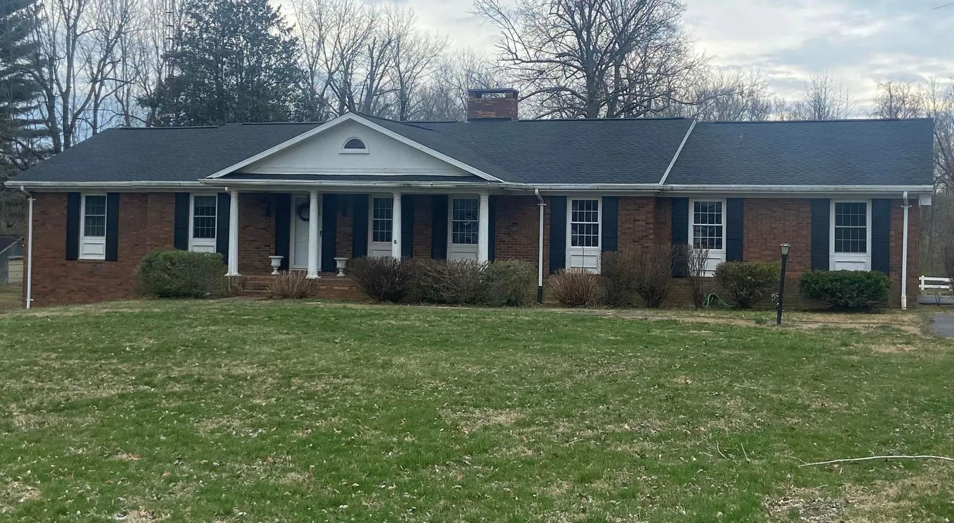 Brick ranch house with black shutters, white columns, and a green lawn.