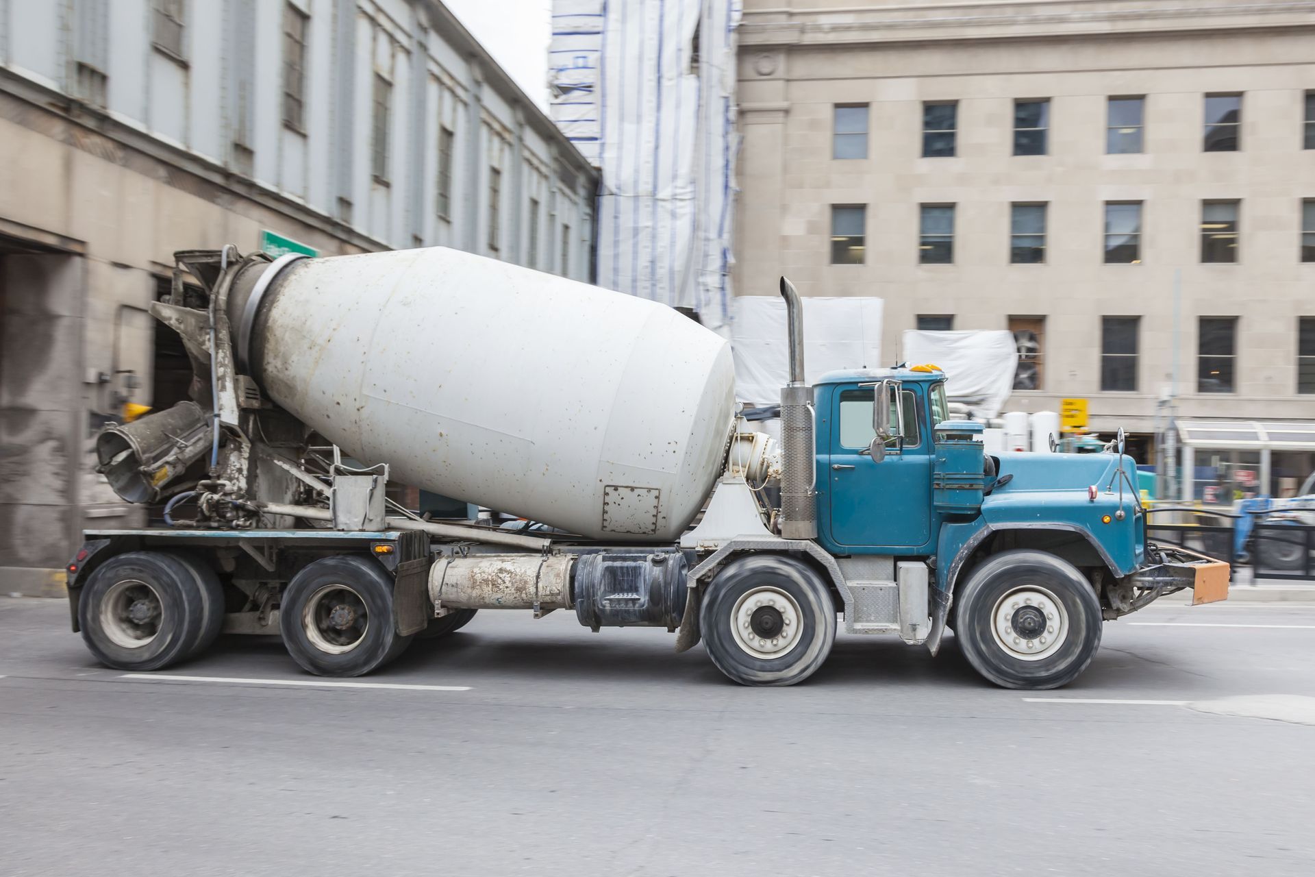 A blue and white concrete mixer truck is parked on a city street next to a large stone building.