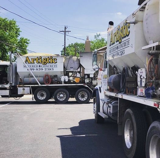 Two Artistic Metered Concrete trucks parked in a lot under a clear blue sky.