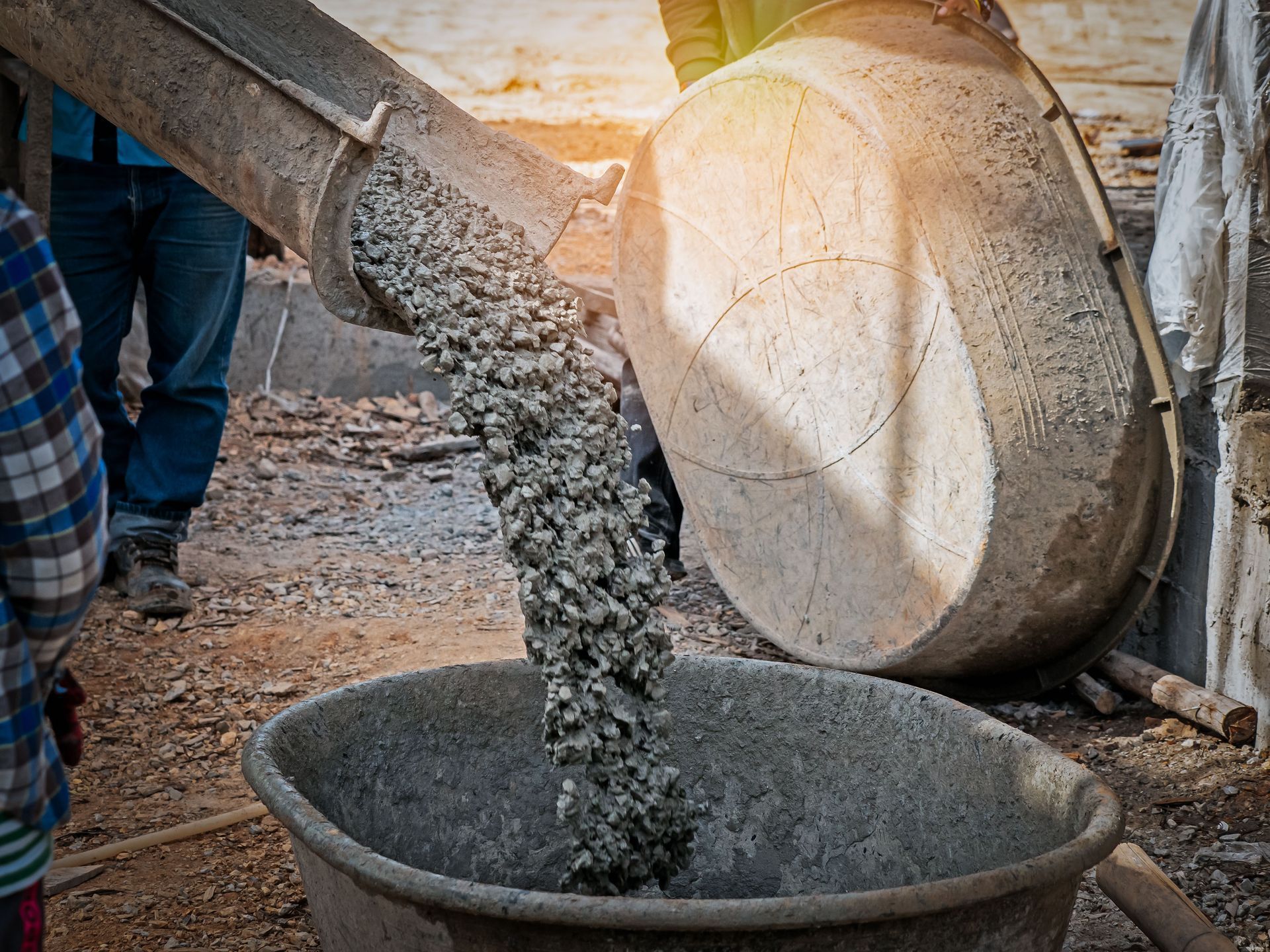 Wet concrete pours from a metal chute into a large wheelbarrow at a construction site.