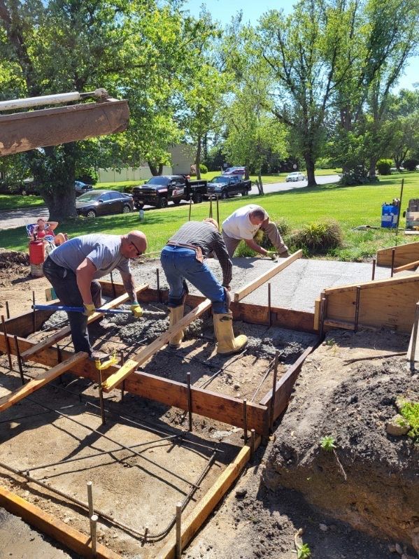 Construction workers level and smooth wet concrete within wooden forms at an outdoor job site.