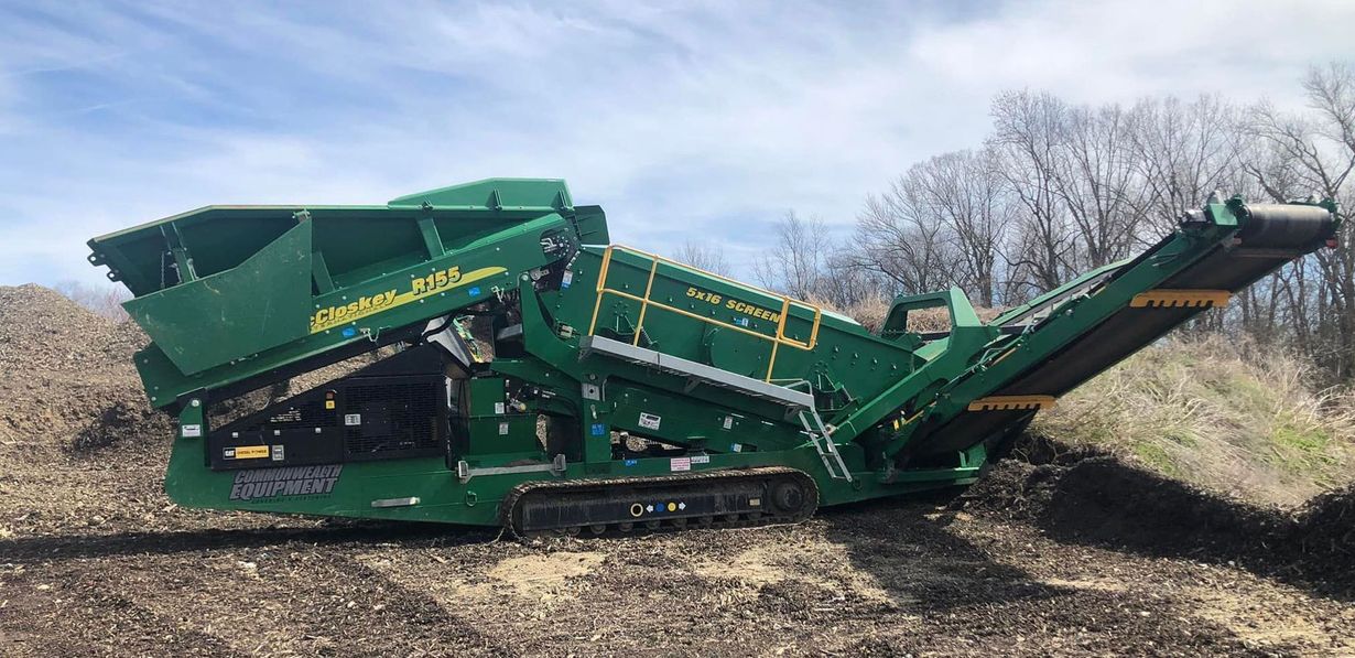 Green track-mounted industrial screening machine sitting on dirt, processing soil outdoors.
