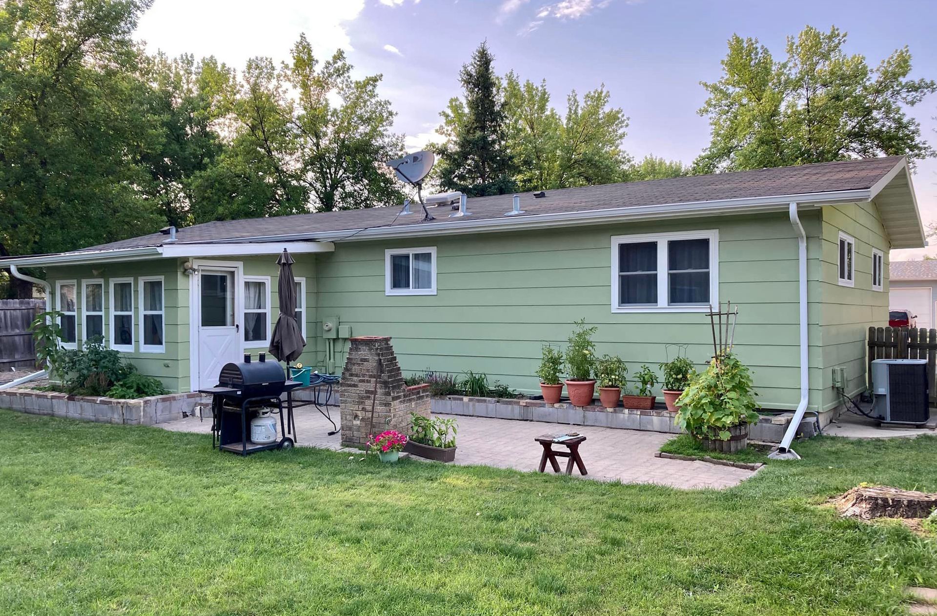 A green house with a grill in the backyard.