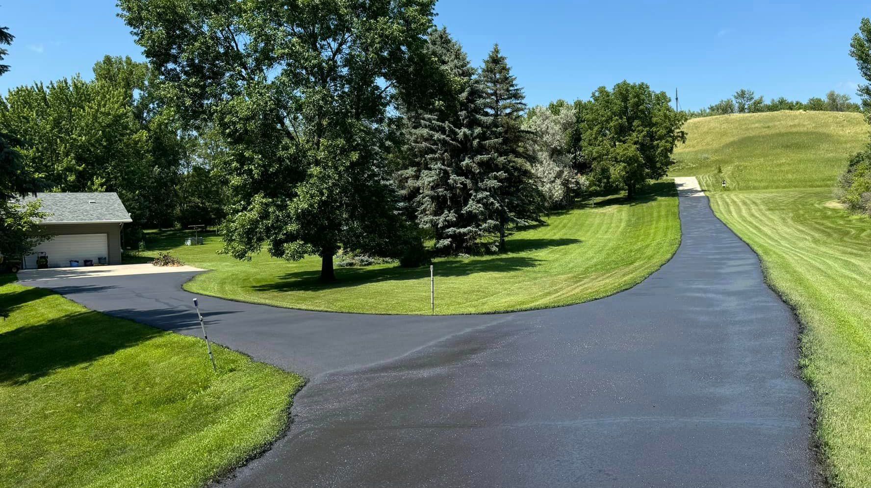 A curvy road going through a grassy field with trees on both sides.