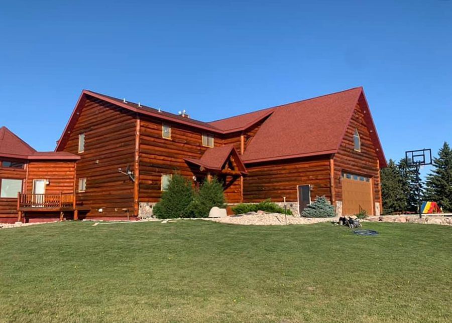 A large log cabin with a red roof is sitting on top of a lush green field.