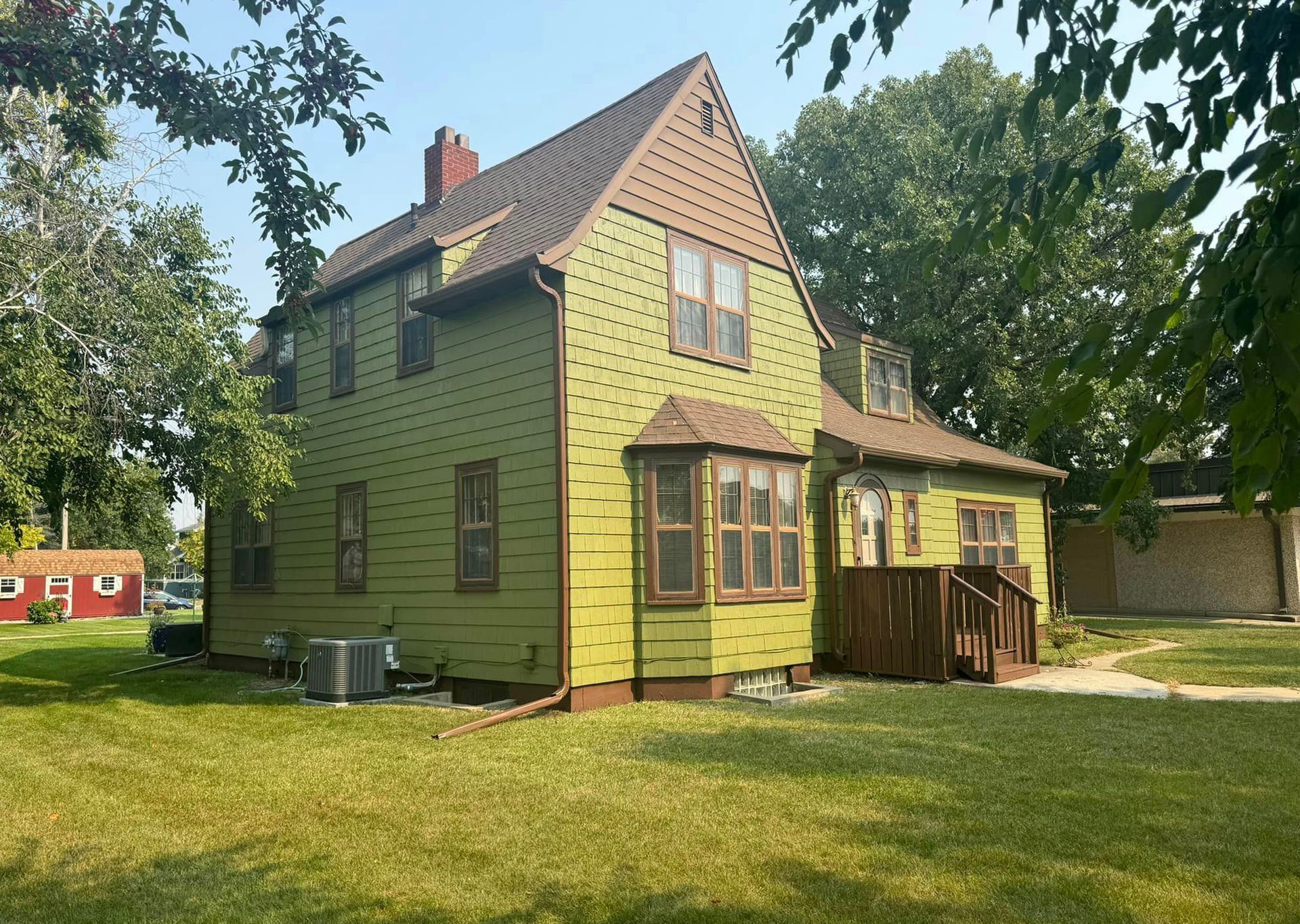 A green house with a brown roof is surrounded by trees