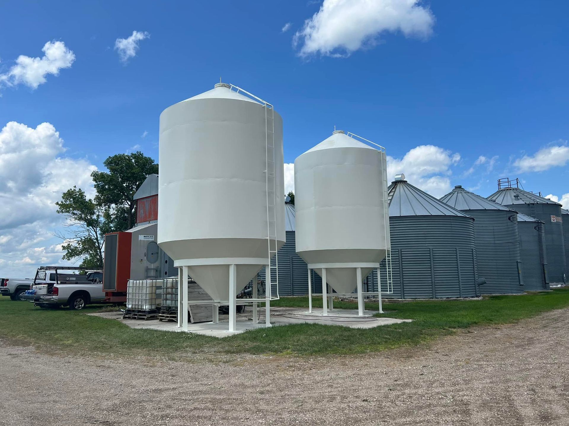 A row of white silos are sitting in a dirt field.