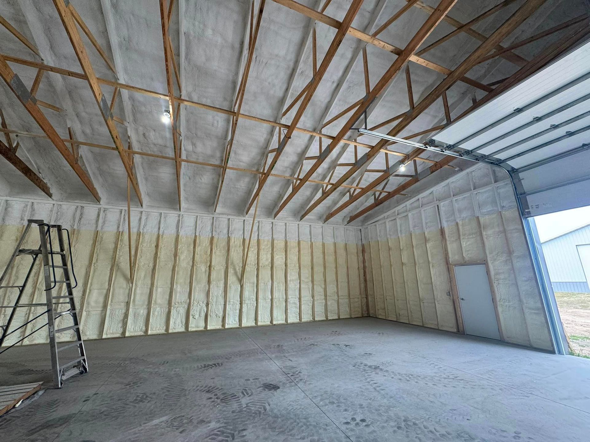 A large empty garage with a ladder and a garage door.