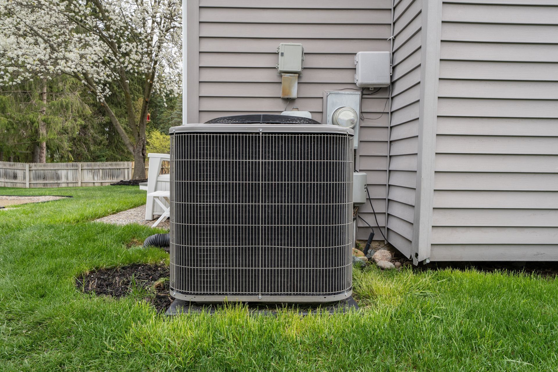 AC unit outside a house with gray siding, surrounded by green grass.
