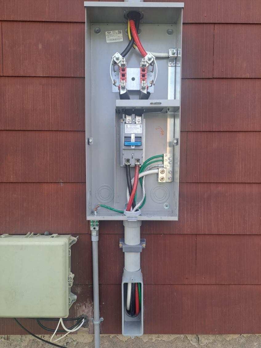 Electrical meter box on a brown siding wall, with wires and conduit visible.