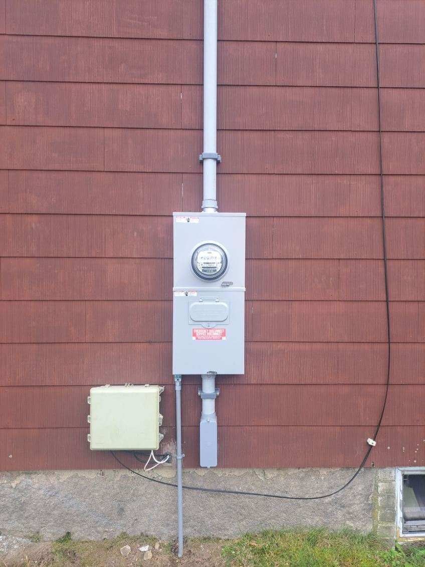 Electrical meter box and conduit on a red clapboard wall with a small utility box and service wire.