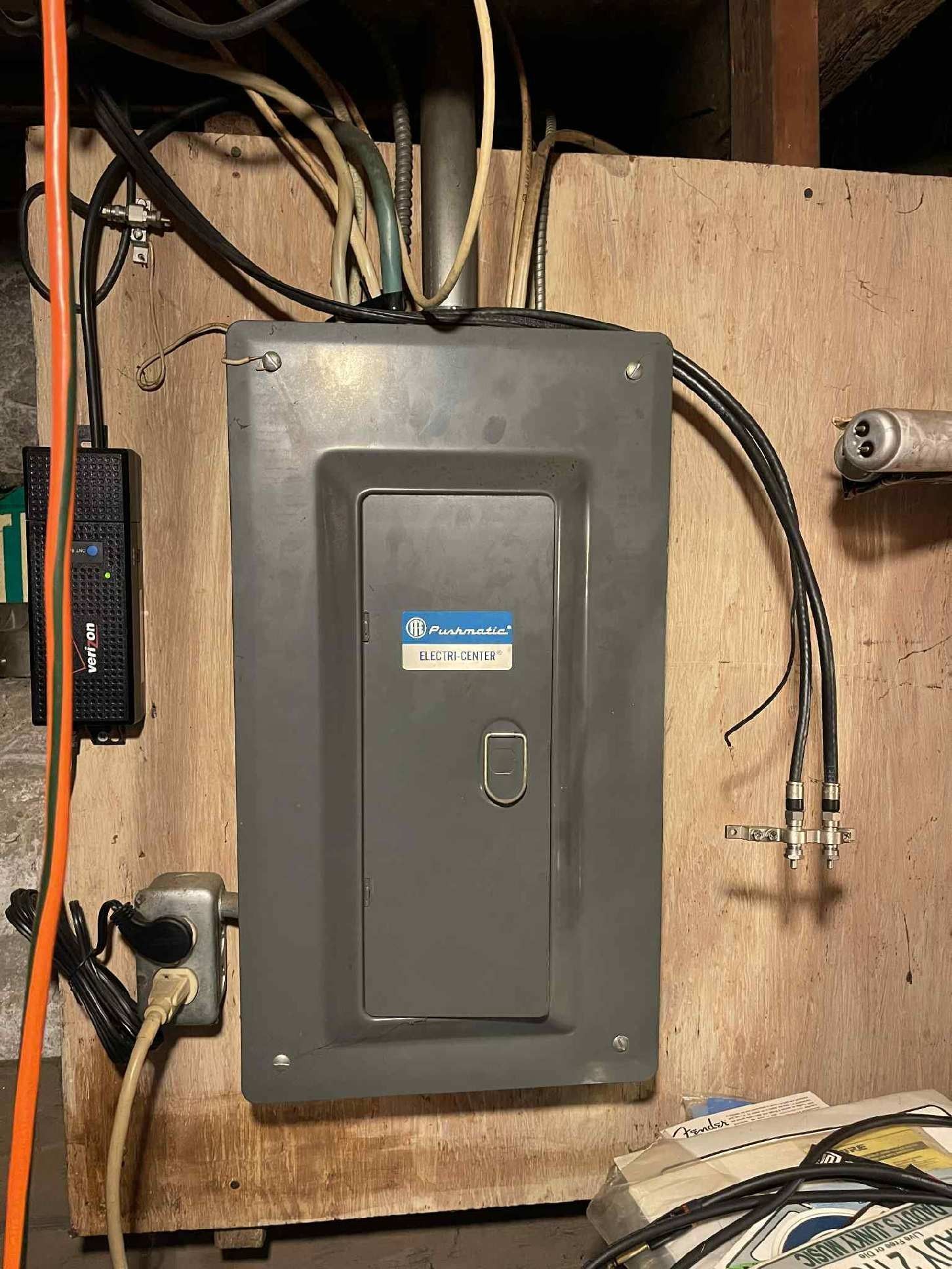 Electrical panel mounted on wood paneling with various wires and cables attached.