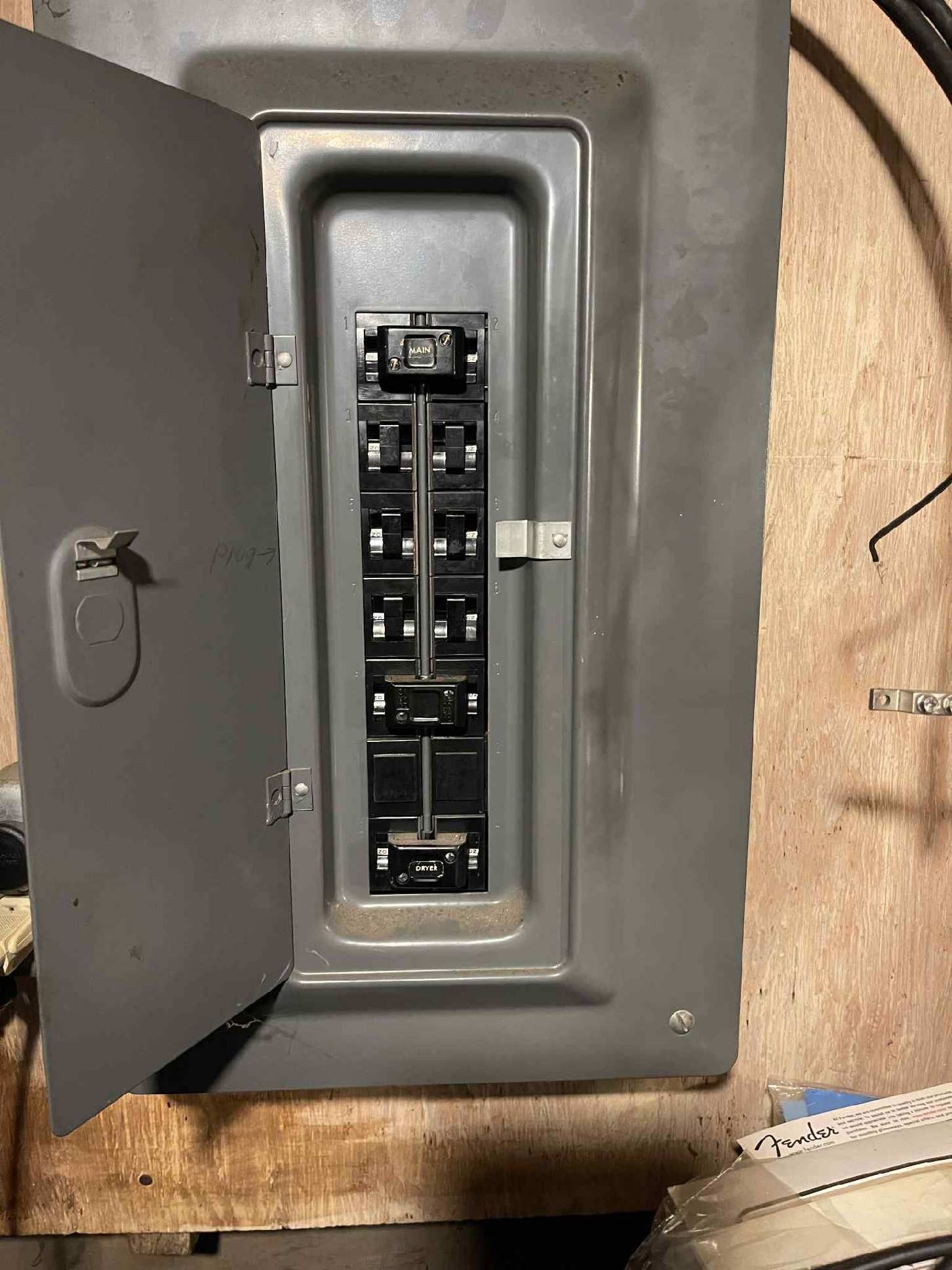 Open electrical breaker panel with various switches. Gray metal box mounted on a wooden wall.