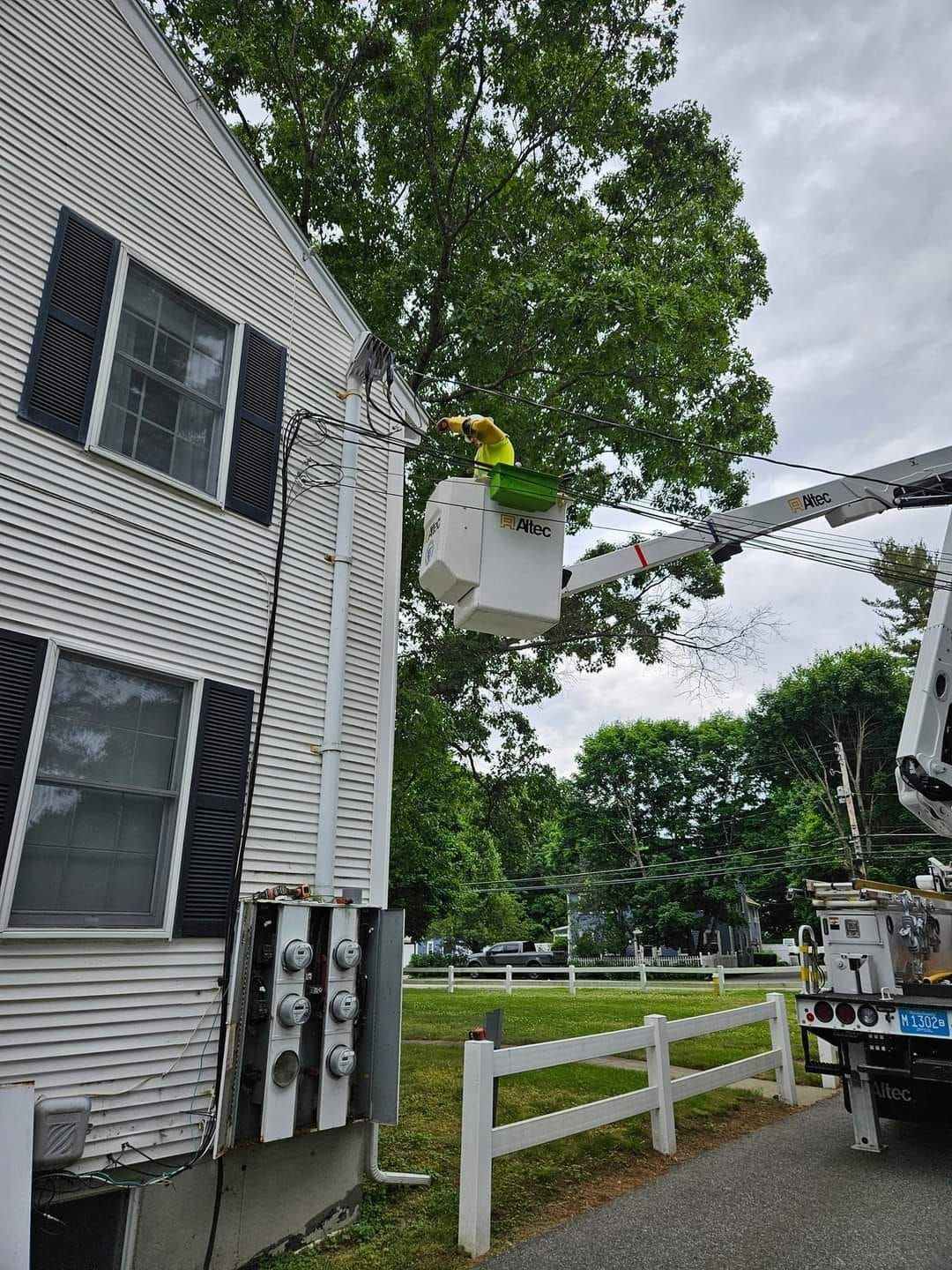 A man in a bucket is cutting a tree in front of a house.