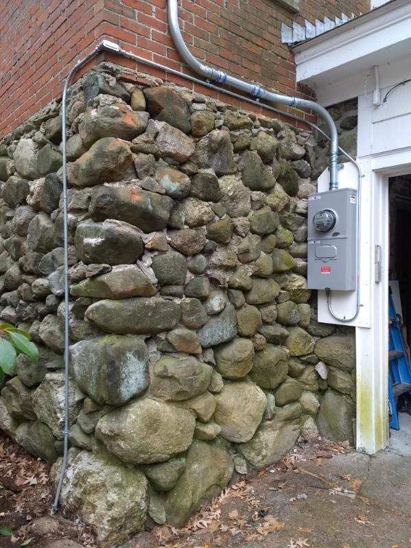A stone wall with a electrical box attached to it.