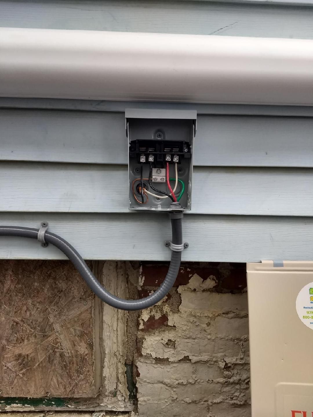 A box with wires coming out of it is attached to the side of a house.