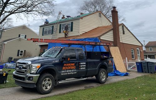 Roofing contractor truck and tarp-covered house roof during repairs, with ladder and debris on lawn.