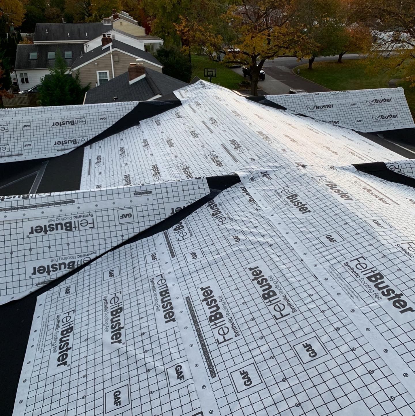 Roof under construction with white underlayment and black seams on a house roof