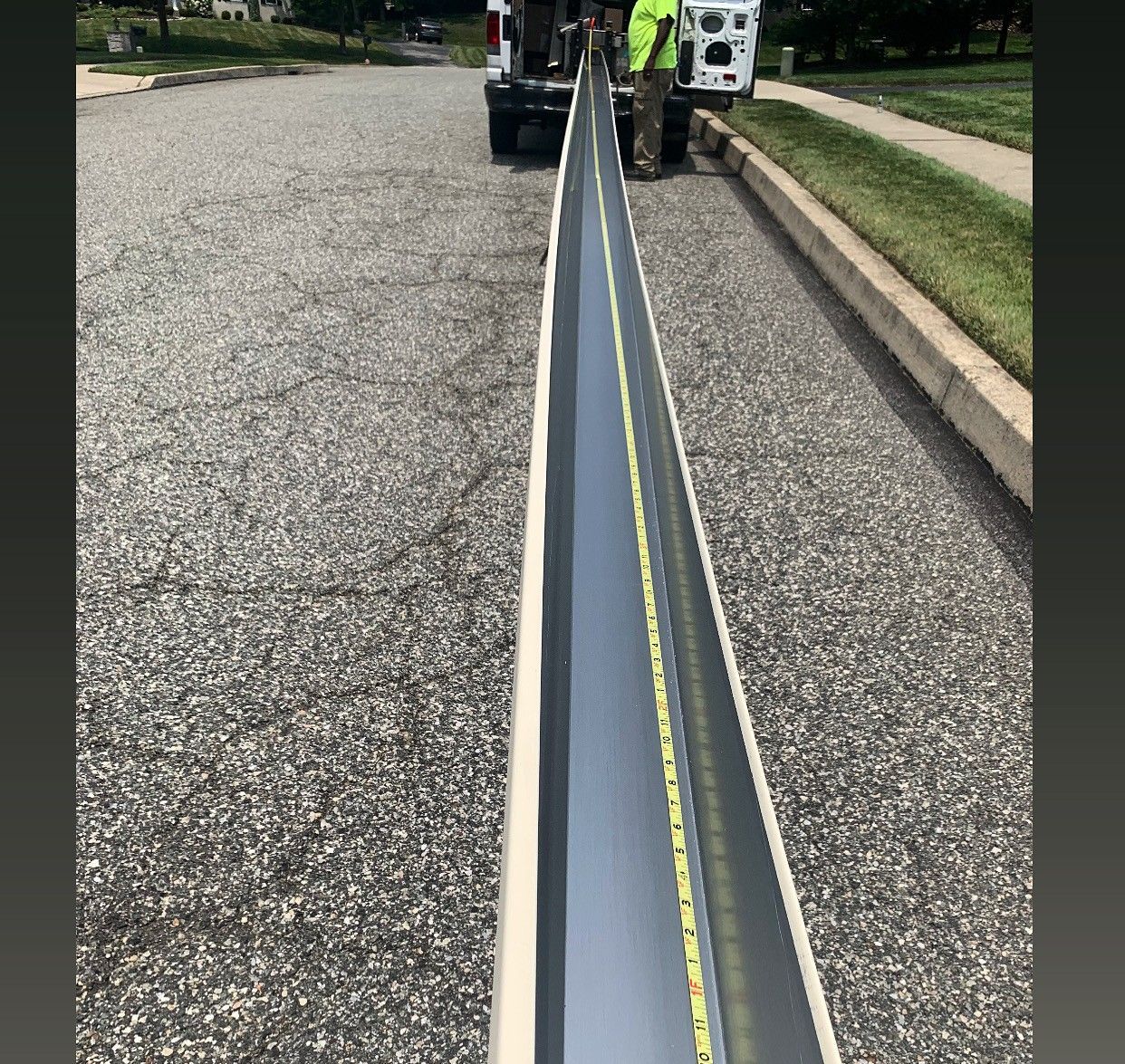 Long metal rail centered on a gravel road with workers and trucks in the distance.