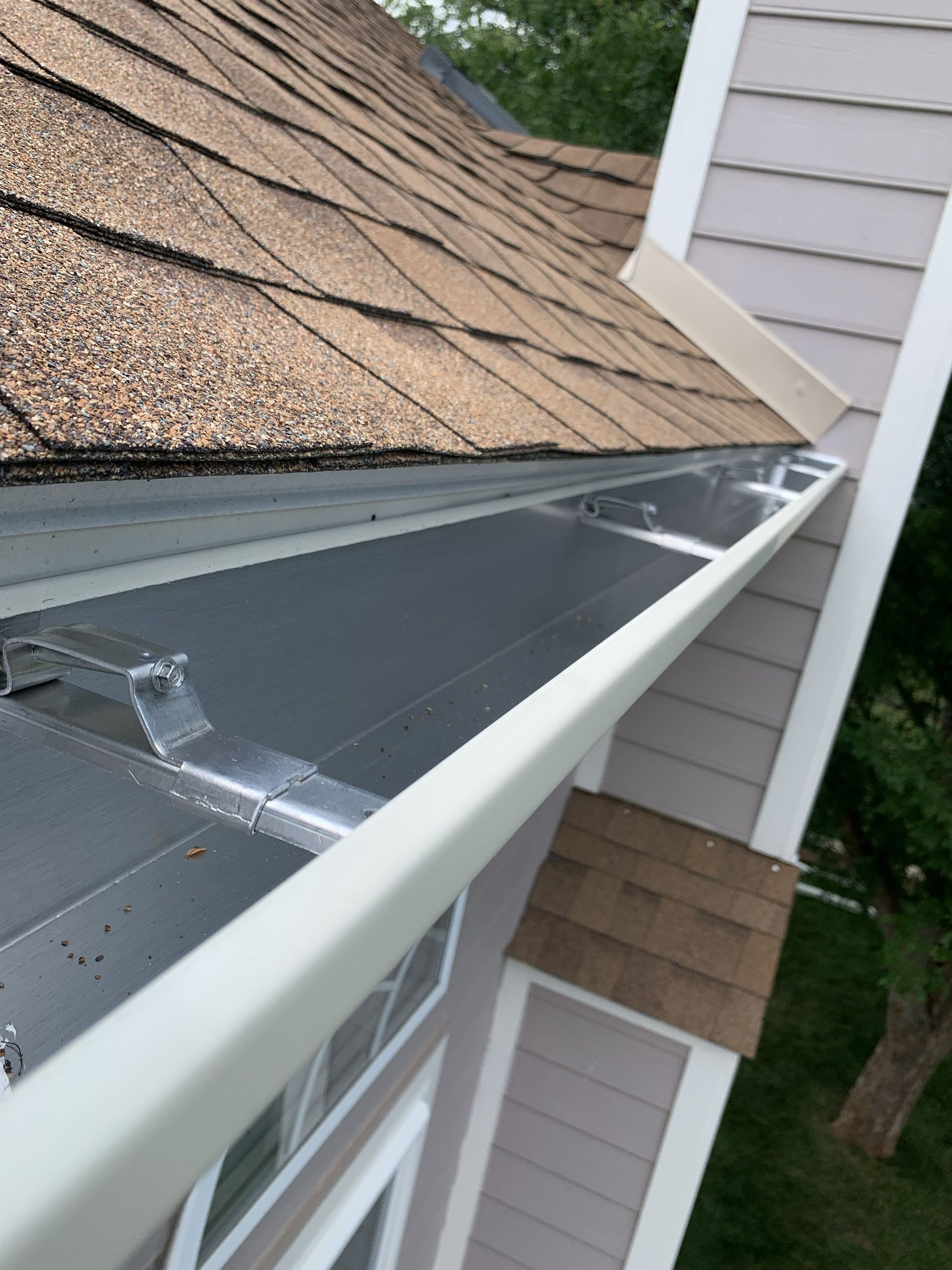 Roof gutter installation along a house roof edge with metal flashing and shingles visible